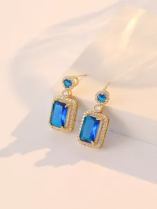 Vue détaillée de boucles d'oreilles dorées avec grandes pierres de zircon bleu