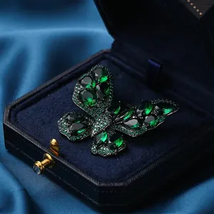 Vintage butterfly brooch with deep green gemstones displayed on elegant blue velvet box