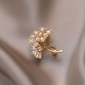 Elegante spilla a foglia di ginkgo dorata con perle e zirconi su sfondo di seta fine