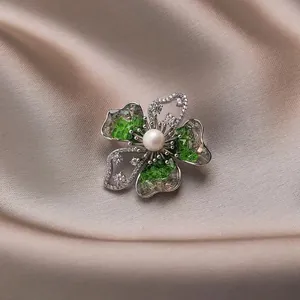 Exquisite flower brooch with green stones and pearl on champagne silk background