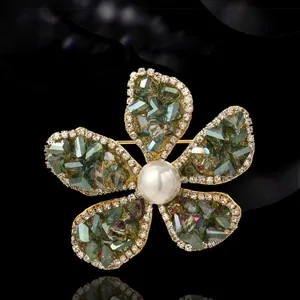 Broche fleur dorée élégante avec cristaux verts et perle blanche centrale sur noir