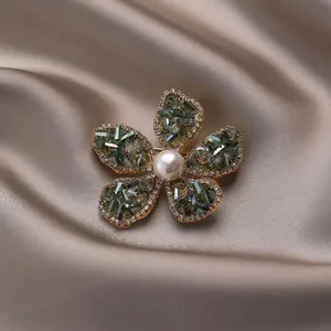 Broche fleur dorée élégante avec pétales en zircon vert et perle sur fond de soie fine
