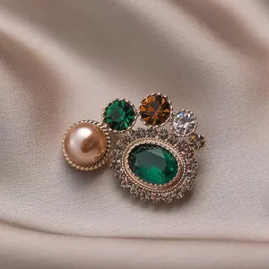 Broche vintage avec émeraude et perle sur un fond de soie couleur champagne