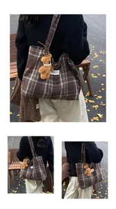 Detail view of large brown plaid tote bag with teddy bear charm on autumn park bench