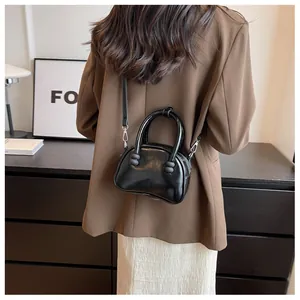 Fashionable black glossy crossbody bag worn by a model in a stylish suit outfit