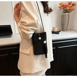 Détail d'un sac à main noir à perles avec pompon floral porté sur un blazer blanc