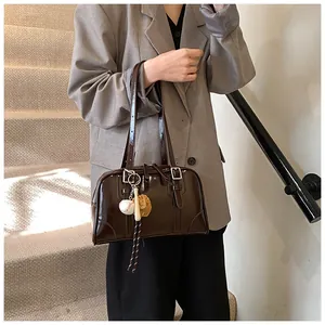 Detail view of dark brown glossy shoulder bag with sports charm on a gray blazer outfit