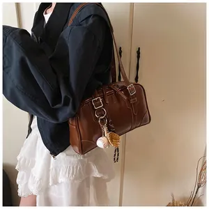 Brown vintage Boston bag with metallic buckle and baseball charm shown on shoulder