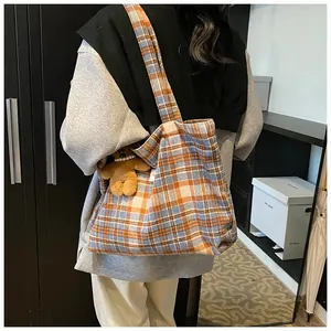 Detail shot of a large plaid tote bag with orange and blue check patterns and bear charm