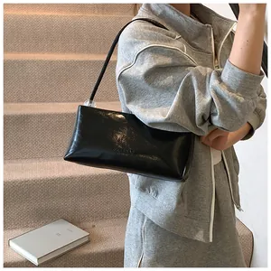 Close-up of black patent leather baguette bag with beaded strap shown on a shoulder