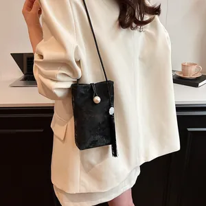 Sac bandoulière noir élégant avec fermoir perle et franges, porté par un mannequin
