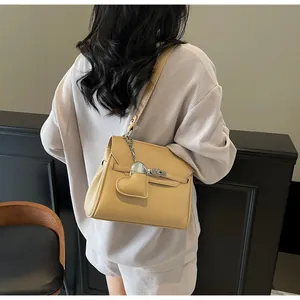 Beige lychee pattern handbag with heart charm and silver metal turn lock shown on model