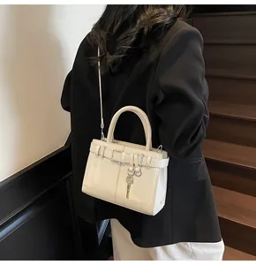 Détail du sac à main crème minimaliste avec pendentif clé dorée et sangle à boucle décorative