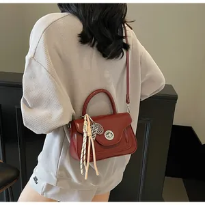 Detail view of burgundy oil-wax leather shoulder bag with tennis racket charm and silver lock