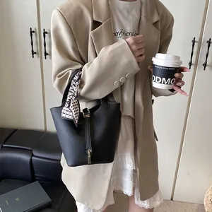 Schicke schwarze Leder-Eimertasche mit Schloss und Seidenschal an einem Büromodell