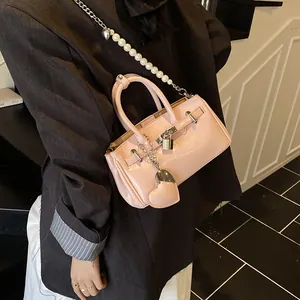 Pink patent leather bucket bag with pearl chain strap and heart charm on a crossbody model