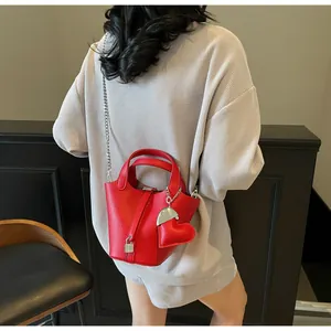 Detail of red lychee leather bucket bag with silver lock and heart pendant on model