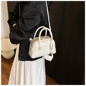Detail of white glossy PU handbag featuring embossed letters and heart-shaped charm