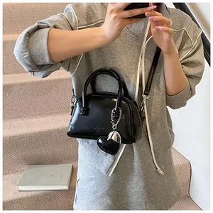 Detail of glossy black leather crossbody bag with silver heart charm and strap