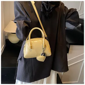 Close-up of pale yellow glossy shoulder bag with heart charm and brand engraving