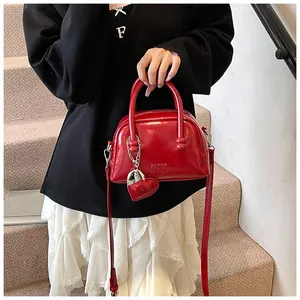 Detailed view of a red patent leather bowling bag with heart charm and crossbody strap