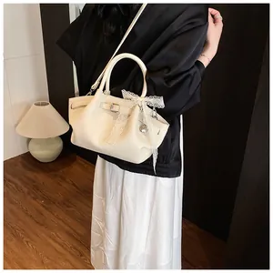 Close-up of cream leather tote bag featuring a lace bow and heart metal charm detail