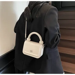 Gros plan d'un sac bandoulière en cuir crème avec poignée arrondie sur un mannequin