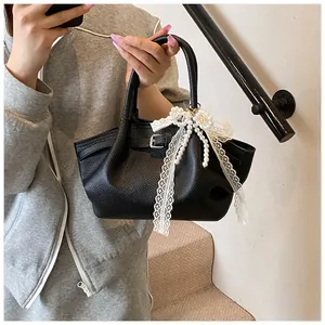 Detail of black pebbled leather tote bag featuring a lace bow and pearl charm ornament