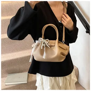 Detail of khaki leather handbag featuring pearl bow ornament and delicate lace pendant