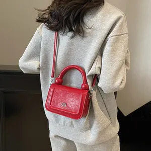 Sac à main chic en cuir verni rouge avec logo argenté porté par un mannequin en sweat gris