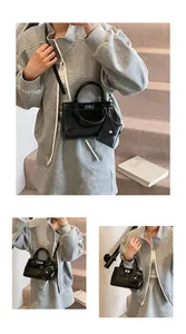 Détail du sac carré noir brillant avec pochette coeur porté par un mannequin