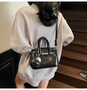 Detail of a glossy black Kelly-style handbag with silver lock and heart charm accessory