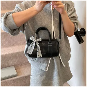 Detail of a shiny black boston bag with decorative polka dot scarf and shoulder strap