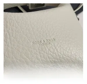 Close-up of off-white lychee grain leather texture and embossed logo on minimalist shoulder bag