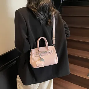 Pink Kelly style handbag with heart charm shown on model in a stylish indoor setting
