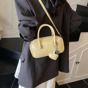 Cream retro bowling handbag with heart charm shown on a stylish charcoal blazer model
