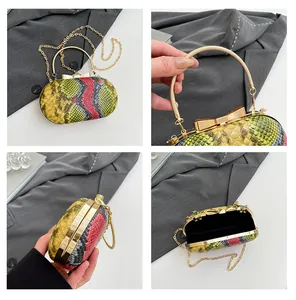 Detail view of oval snakeskin pattern clutch with gold handle and chain shoulder strap