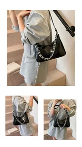 Detail of a shiny black patent leather crescent bag with bold silver metal chain decor