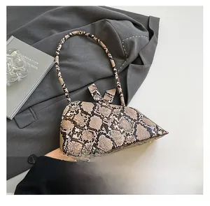 Vue détaillée du sac à main serpent avec clous dorés posé sur une veste de costume grise