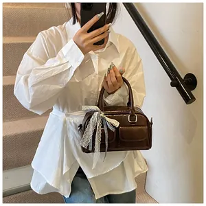 Detail of dark brown faux leather shoulder bag featuring side rings and decorative bows