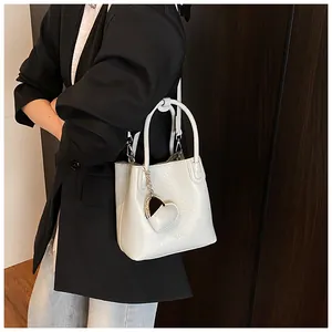 Close-up of white lychee leather bucket bag with heart pendant and top handle
