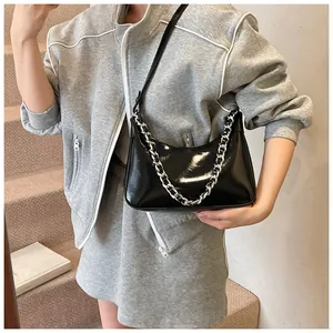 Detail of black glossy hobo bag with silver chain strap worn by a model in interior setting