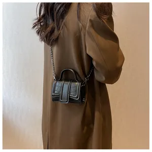 Detail of a mini black faux crocodile crossbody bag with metal chain on a model