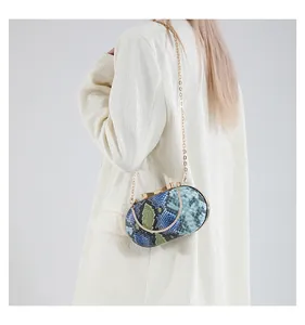 Detail of blue-green snakeskin pattern clutch bag with gold butterfly clasp worn by model
