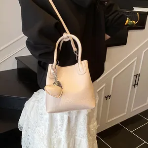 Minimalist beige bucket bag with lychee texture and heart charm shown on a model