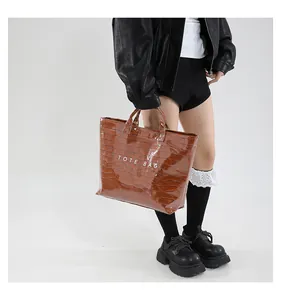 Detail of glossy crocodile pattern on brown tote bag with TOTE BAG lettering