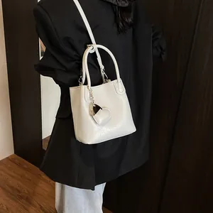 White leather bucket bag with silver heart charm worn by model over a black blazer
