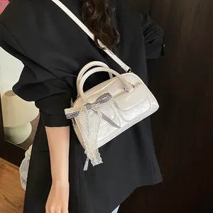 Chic cream shoulder bag with lace bow charm and glossy finish in a lifestyle setting