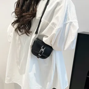 Minimalistische schwarze Mini-Umhängetasche aus Leder mit Silberschnalle auf weißem Hemd