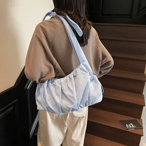 Light blue pleated cloud bag with wide shoulder strap shown on model by wooden stairs